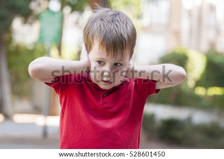 Little Caucasian boy in red polo shirt closing ears with his hands. Child does not want to hear. Protective pose, protectiveness, childhood traumatic experience. Royalty-Free Stock Photo #528601450
