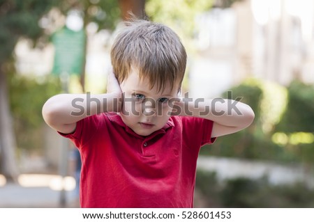 Little Caucasian boy closing ears with his hands and looking at the camera. Childhood traumatic experience, psychology, psychological, protective behavior, conduct, protectiveness. Staring Royalty-Free Stock Photo #528601453