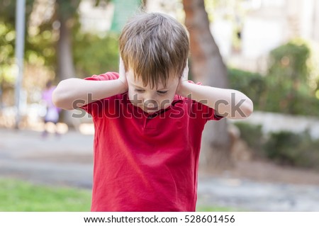 Little Caucasian boy closing ears with his hands in a protective position. Childhood traumatic experience, psychology, psychological, asperger syndrome, asperger's disorder, autistic, autism. Royalty-Free Stock Photo #528601456