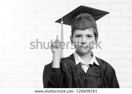 Primary school boy in cup and gown showing up with his finger.