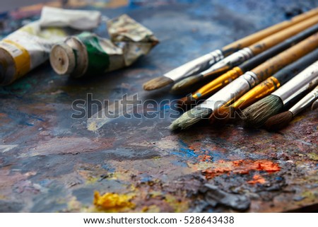 Oil paints and paint brushes on a palette close up. Royalty-Free Stock Photo #528643438