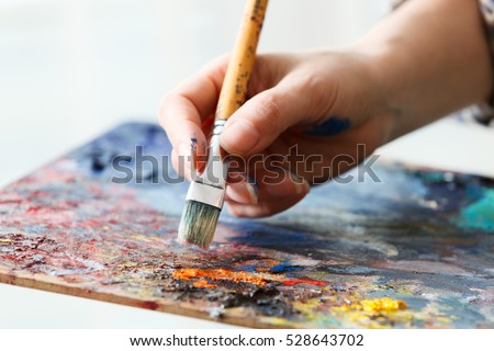 Artist paints a picture of oil paint brush in hand with palette close up. Royalty-Free Stock Photo #528643702