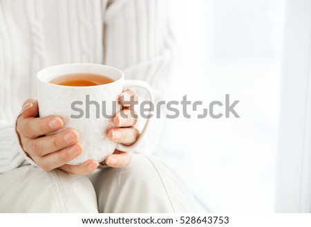  Woman's hands is holding hot cup of coffee or tea in morning sunlight. Royalty-Free Stock Photo #528643753