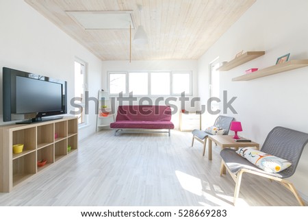 scandinavian minimalistic interior in wooden cottage with white wooden floor and white wooden ceiling and white painted walls living room with pink coach and grey chairs. Royalty-Free Stock Photo #528669283