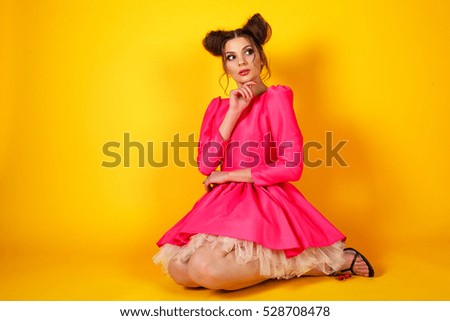 Playful and stylish brunette girl in the image of the doll on a yellow background. Woman looks like a doll. An unusual image for a party.