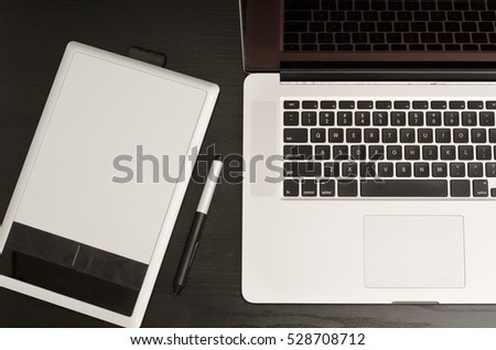 Graphics tablet with a pencil, some laptop on black wooden table, close-up