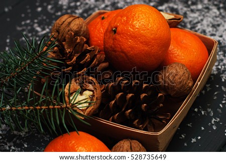 Christmas concept - basket of tangerines, walnuts and pine cones on gray snowy wooden background