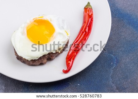 Beefsteak with fried egg and chili pepper on blue background. Top view. Selective focus.