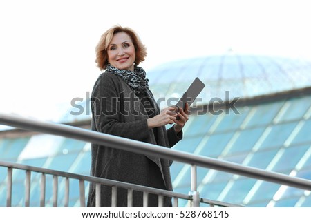 Gorgeous middle aged businesswoman holding tablet, outdoors