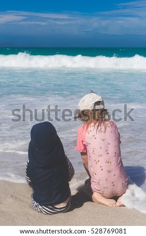 two small kids wearing bright sun protective swimming clothes and sitting in sands and playing together with coming atlantic ocean waves 