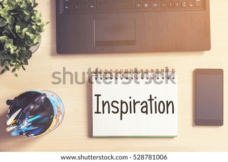Notebook with text inside Inspiration on table with laptop, mobile phone and plant