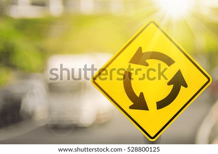 Roundabout warning sign on blur traffic road with colorful bokeh light abstract background. Copy space of transportation and travel concept. Retro tone filter color style.