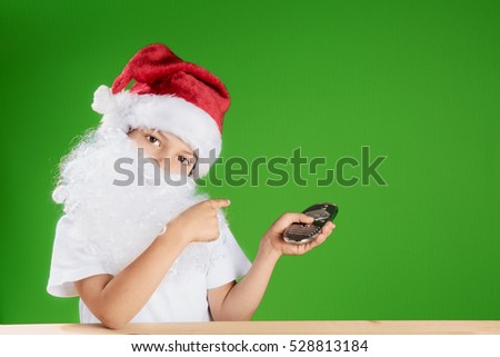 Young Santa Claus sitting at a wooden table and talking on the phone. Holding a blank picture frame with white background. Blue background. Chromakey. Closeup.