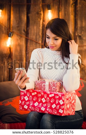 Pretty woman taking selfie photo on mobile phone near decorated christmas wall with light bulbs