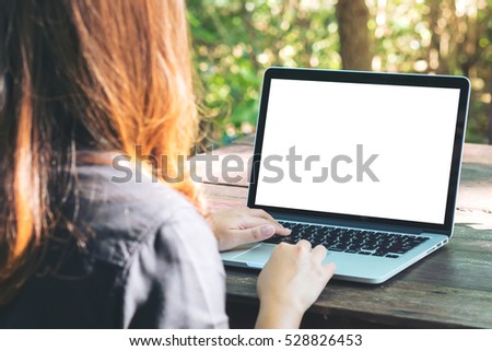 Mockup image of a woman using laptop with blank white screen on vintage wooden table in nature outdoor park
