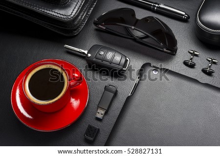 Man accessories in business style with cup of coffee, gadgets, car key, cufflinks, sunglasses, briefcase and other luxury businessman attributes on leather black background, fashion industry Royalty-Free Stock Photo #528827131