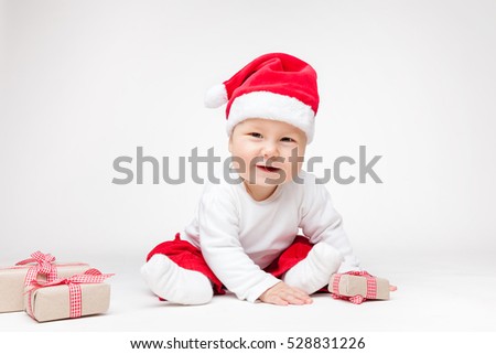 Adorable young baby boy wearing a Santa hat opening Christmas presents