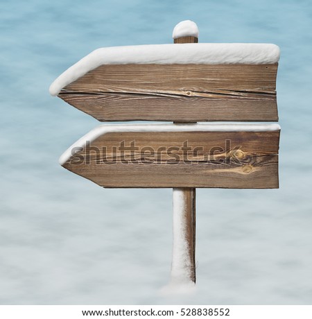 Wooden direction sign with less snow on it and snow on background. two arrows in one direction