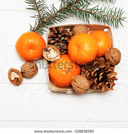 Christmas concept -?? basket of tangerines, walnuts and pine cones with fir branch on white wooden background