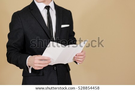 Man showing blank black flyer brochure. Read detailed booklet. Leaflet presentation. Pamphlet hold hands. Man show clear offset paper. Sheet template. A man in a black suit, white shirt and tie