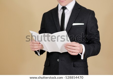Man showing blank black flyer brochure. Read detailed booklet. Leaflet presentation. Pamphlet hold hands. Man show clear offset paper. Sheet template. A man in a black suit, white shirt and tie