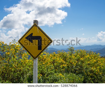 Yellow turn left sign and blue sky, flower background