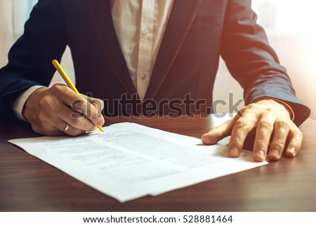Man businessman signs documents with a pen making the signature sitting at the desk in the light. With retro effect.