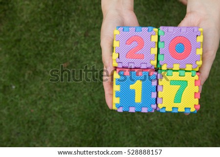 Woman hold toy puzzle wording 2017 on hand with green grass background
