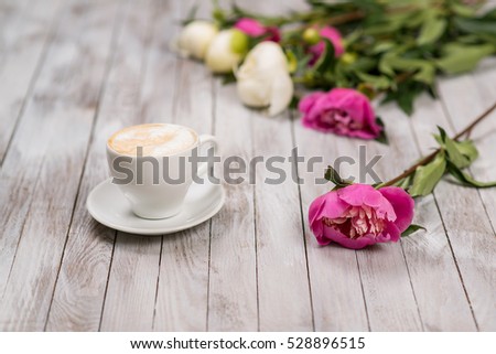 A bouquet of peonies and cup of coffee on light wooden background.