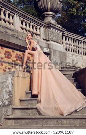 fashion outdoor photo of gorgeous young bride with dark hair in elegant wedding dress posing beside old castle