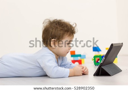 Toddler baby watching cartoons on her tablet computer in the background of the toys he child does not want to play