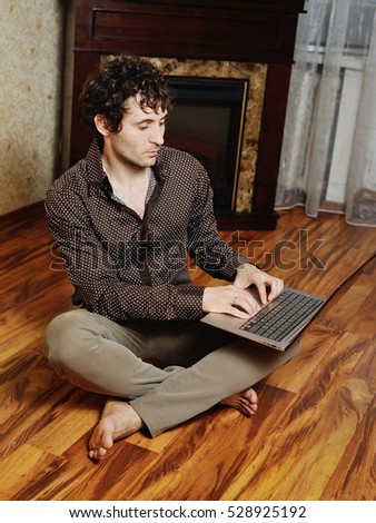 cute young boy with curly hair sitting barefoot at a laptop on the floor on a background of fire