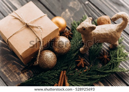 Cute paper cat toy near rustic eco christmas present on wooden background, golden tree ornaments, cinnamon sticks, anise and tree branch on table