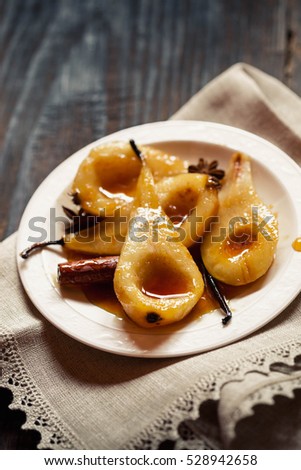 Caramelized Pears - Poached pears with spices in syrup on the white plate on a dark wooden table. Delicious dessert for holiday. Top view