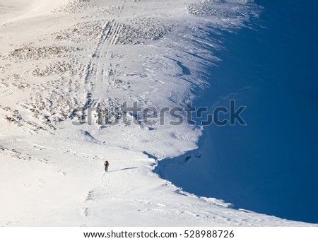 A tourist with a backpack walking the snowy mountains.It is clear seen  scale of large mountains and small man