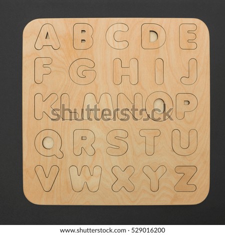 Wooden board with the English alphabet letters and wood. 
Sorter toy for child development and education and learning the alphabet, isolated on black background.