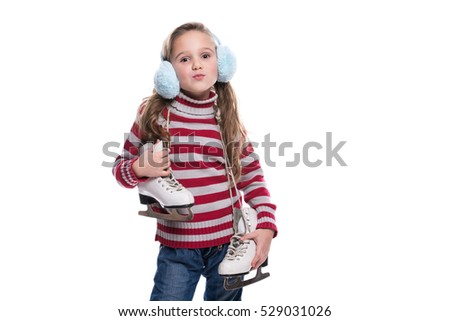 Lovely smiling little girl wearing colorful striped sweater and headdress, holding skates isolated on white background. Winter clothes