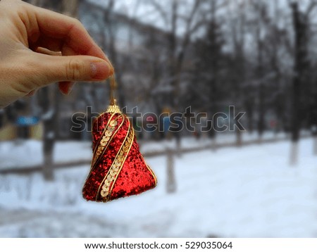 Hand holds a beautiful Christmas ball with red ribbon on a blurred background of a winter snowy landscape