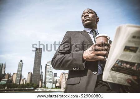 Confident businessman. Successful young man in full suit reading financial news on newspaper and drinking a cup of coffee