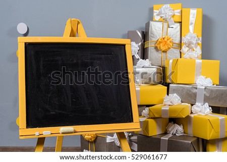 a empty yellow tripod on wooden floor with grey wall and heap of yellow and grey christmas gift box