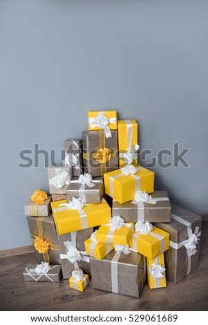 A pile of yellow and grey Christmas gifts with ribbons against the wall on a beautiful hardwood floor with copyspace