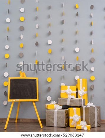 A pile of yellow and grey Christmas gifts in colorful wrapping with ribbons against the wall on a beautiful hardwood floor with copyspace