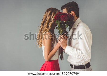 Beautiful elegant couple is kissing behind roses, on gray background Royalty-Free Stock Photo #529070749