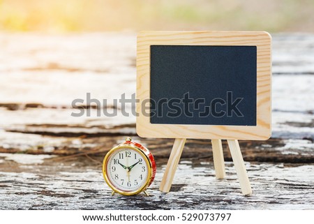 Blank small blackboard with alarm clock on grunge wooden table