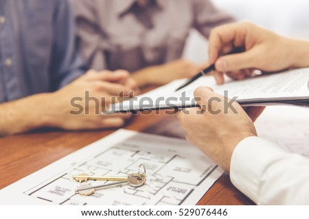 Cropped image of beautiful couple talking with realtor, who is showing where to sign the documents Royalty-Free Stock Photo #529076446