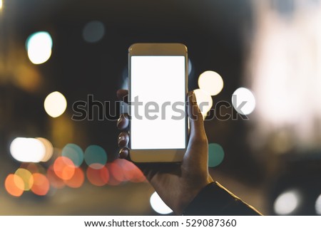 Girl holding on blank screen smartphone on background illumination glow bokeh light in night atmospheric christmas city, hands using template mobile phone on lights auto and glitter street; mockup