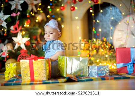 beautiful little girl, holds the Christmas gift in hand. Bright festive fires on a background. Waiting for a holiday.