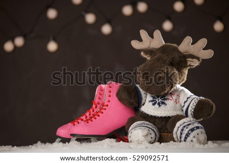 Merry Christmas and Happy New Year. Pink skates for figure skating and toy elk or deer on the snow over dark background.