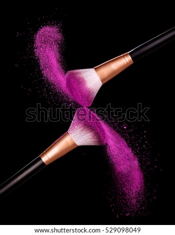 Make-up brush with pink powder dust on black background