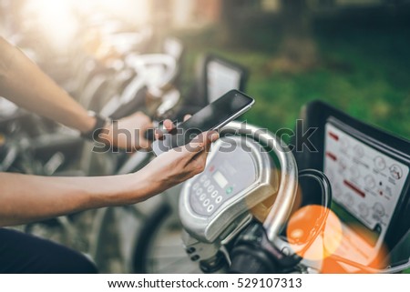 Side view. Close-up of smartphone with blank screen in hand of young woman sitting on city bike.Girl pays with smartphone rent bicycle. Girl using gadget.Film effect. Eco-friendly transport.